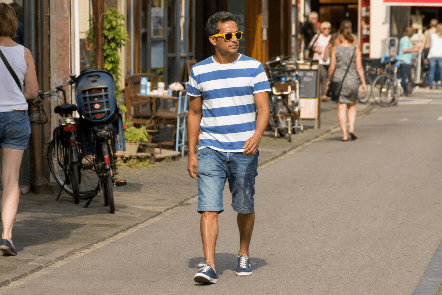 Hombre con camiseta azul y blanca a rayas, bermudas de mezclilla y sneakers